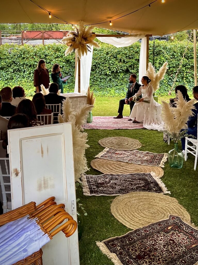 Tamara y Diego durante su ceremonia de boda bajo un altar decorado con pampas