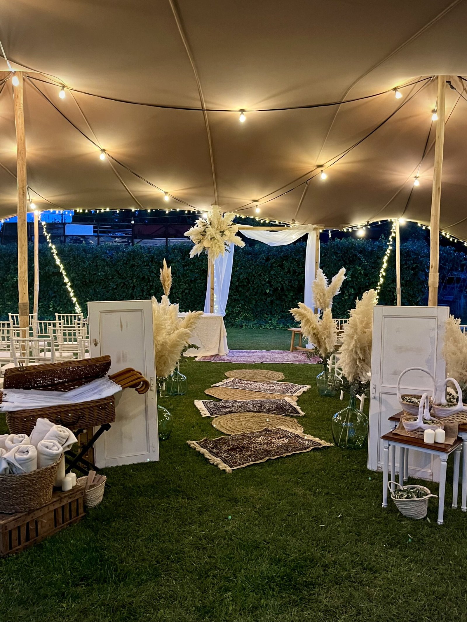 Entrada de una ceremonia de boda decorada con alfombras, pampas y luces en La Almenara de Copau