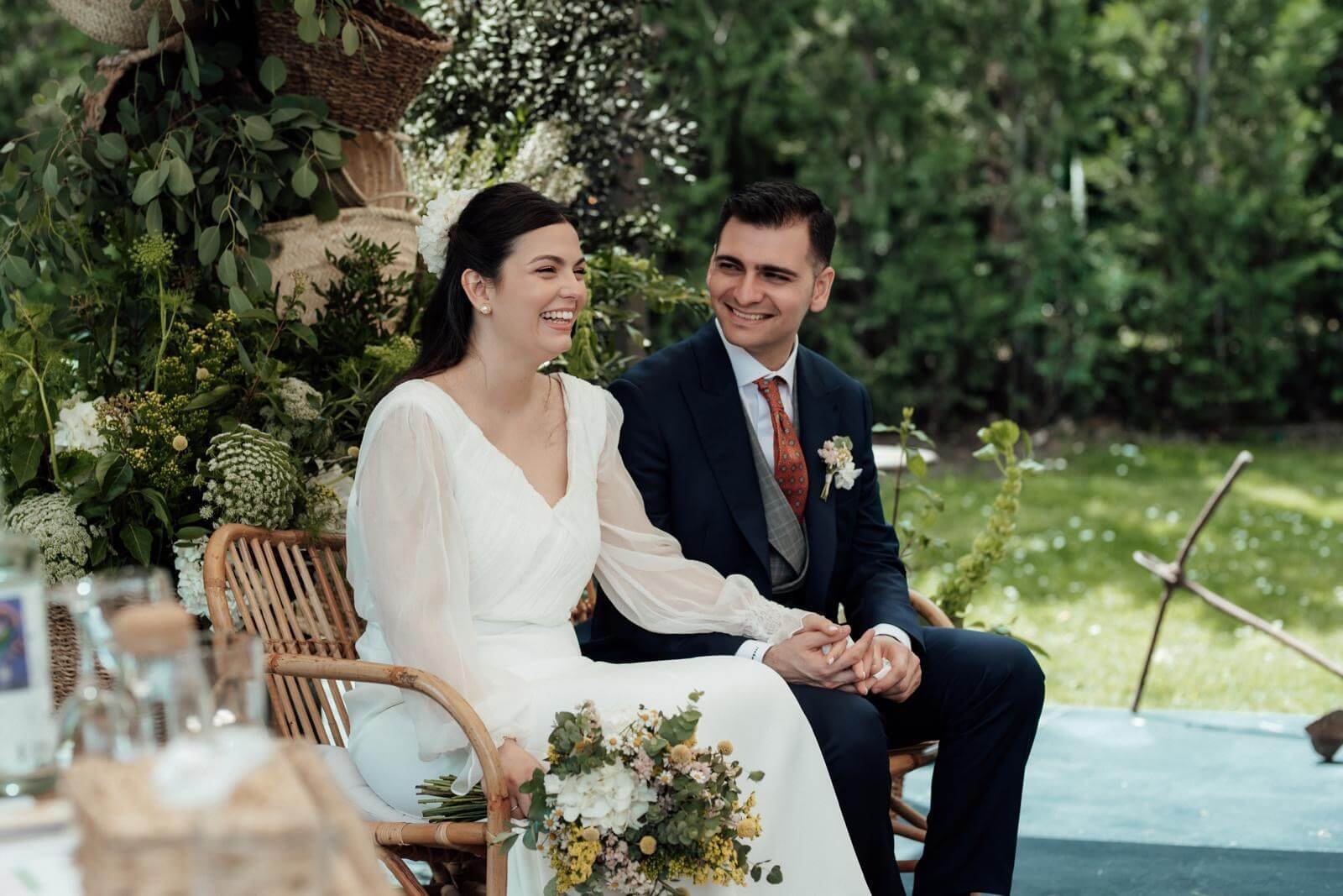 Raquel y Andrés sentados juntos y sonrientes durante la ceremonia de su boda