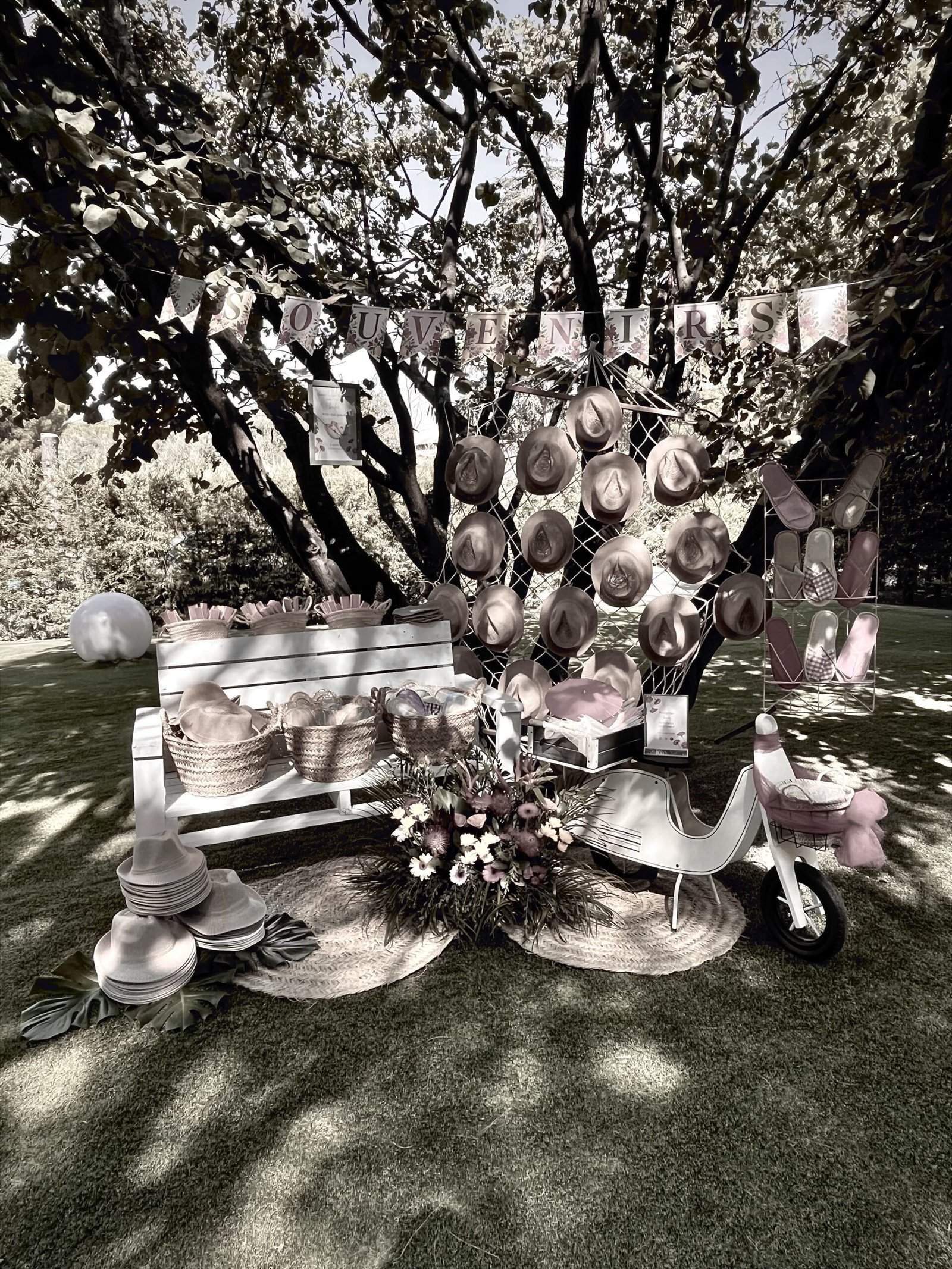 Decoración de bodas en Zaragoza: rincón de sombreros de paja colgados bajo un árbol, con banco blanco, cestas y flores