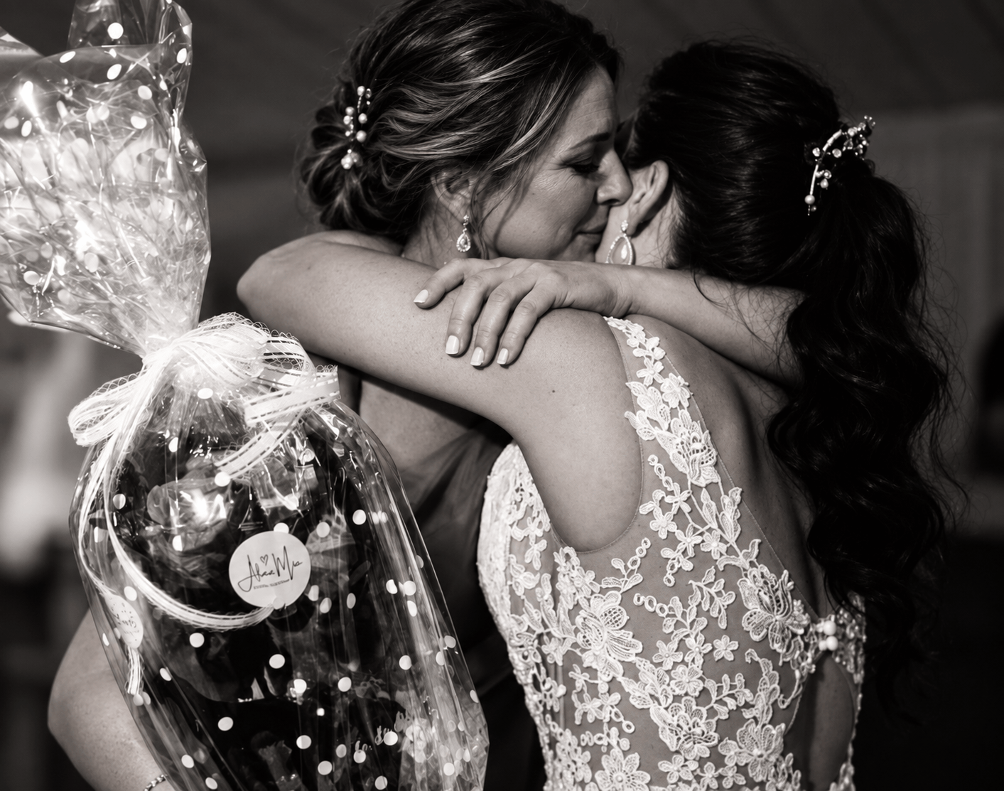 Regalos personalizados para boda: la novia abraza a una invitada que sostiene un regalo envuelto con etiqueta personalizada