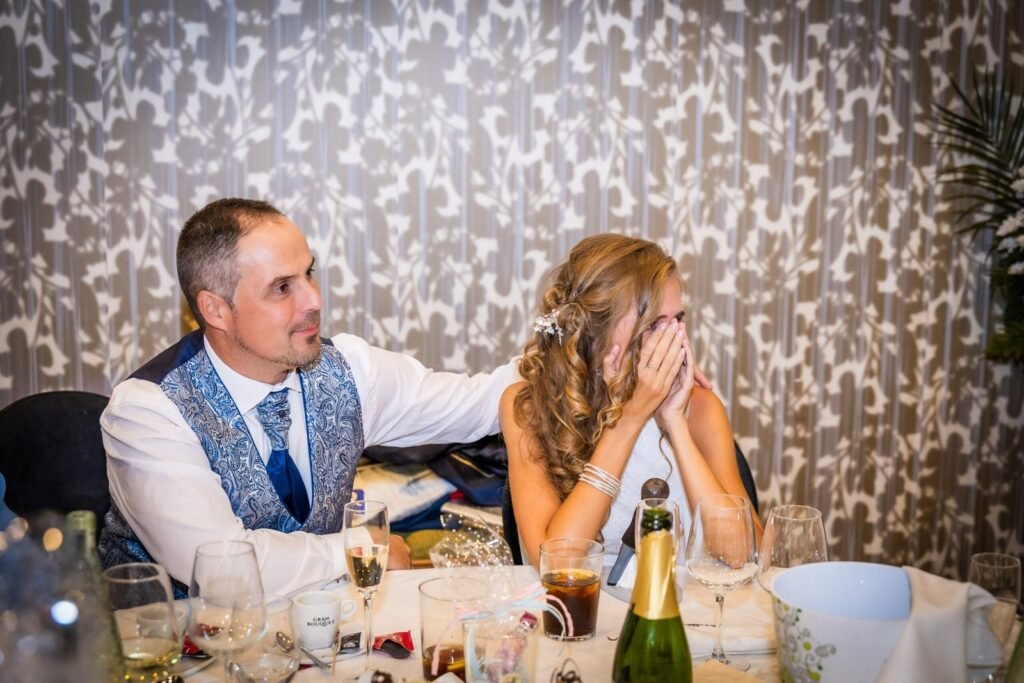 Novia emocionada se tapa la cara mientras el novio la abraza durante los discursos del banquete en Restaurante Aura Zaragoza.